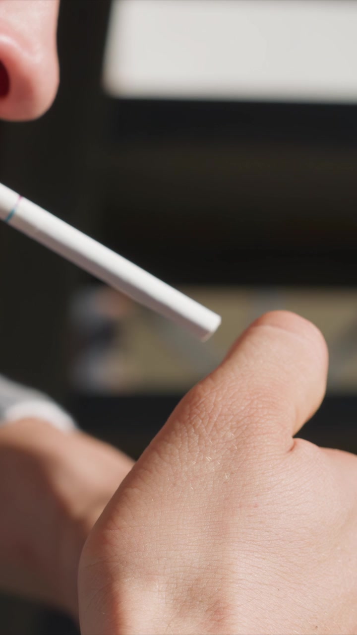 Primo piano della mano di una persona che tiene una sigaretta elettronica, con texture e dettagli della pelle visibili. Lo sfondo è sfocato, concentrandosi sull'interazione tra il dispositivo e le dita. L'illuminazione soffusa evidenzia.