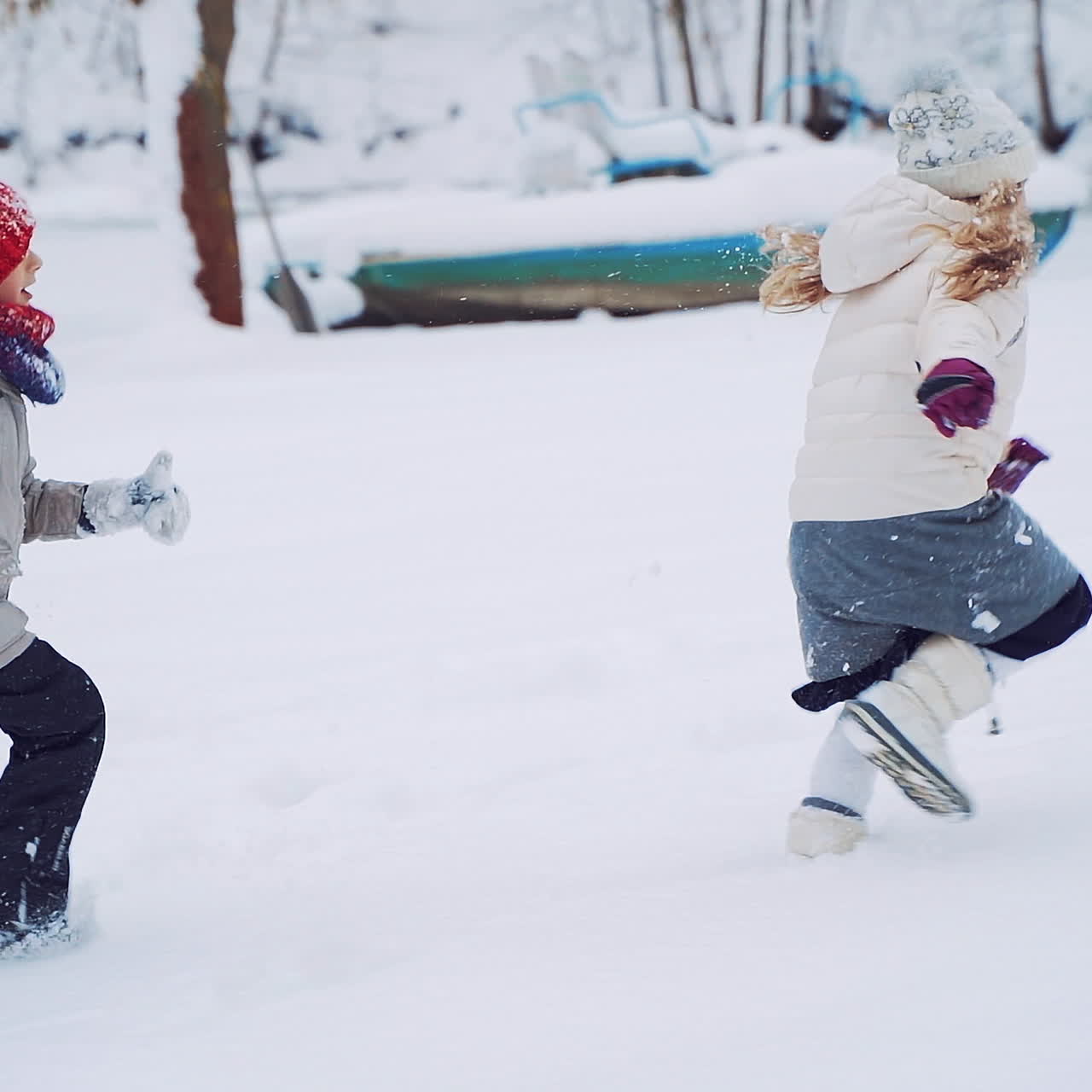 Side view of two children in warm clothes and caps are running on the snowy background. Active kids are playing in winter near the forest. Slow motion.
