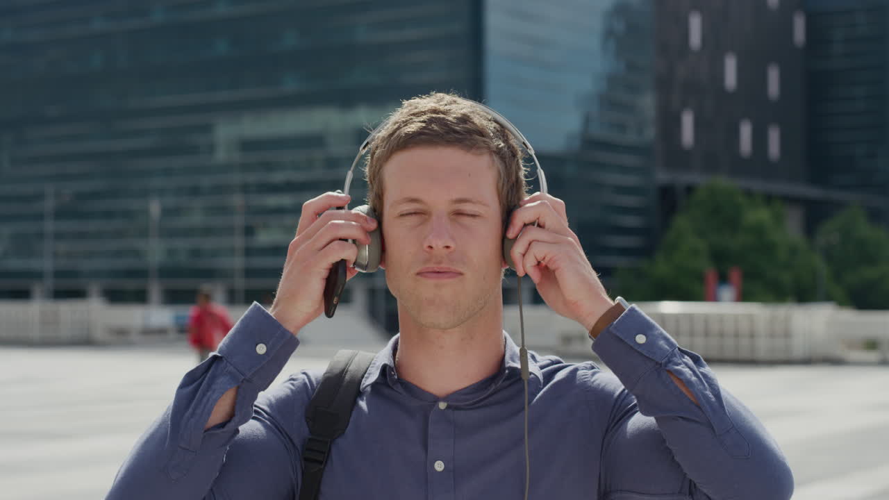 portrait attractive young man puts on headphones listening to music in city enjoying relaxed urban lifestyle on sunny day slow motion