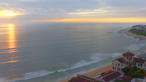 Sunrise-sunset-drone-JBay-Jefferson-Bay-best-surf-spot-in-world-South-Africa-orange-bright-golden-yellow-sun-reflect-water-horizon-waves-stunning-coastline-with-beach-home-buildings-cinematic-forward