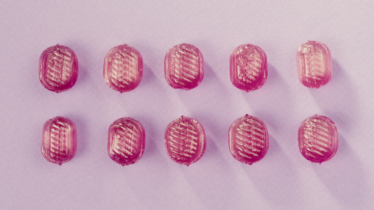 Pink lollipops, candies, bonbons with glitter sprinkles on purple background. Summer bright texture studio shot for store, supermarket, close up top view. Children's favorite sweets made of sugar.