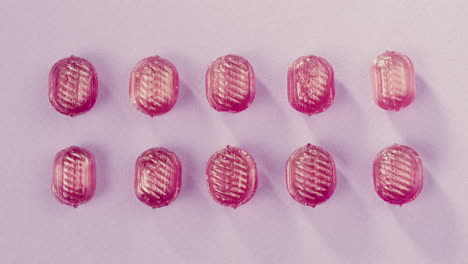 Pink lollipops, candies, bonbons with glitter sprinkles on purple background. Summer bright texture studio shot for store, supermarket, close up top view. Children's favorite sweets made of sugar.
