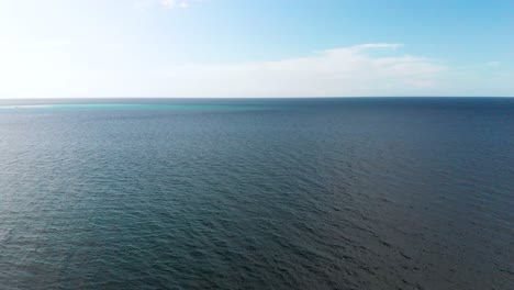 drone aerial over dark ocean water under blue sky and white clouds