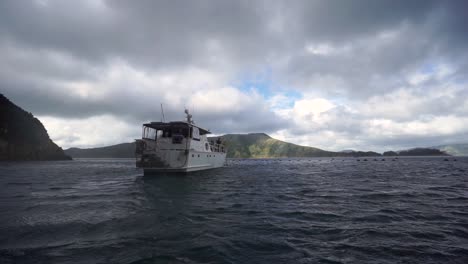 SLOWMO---Cruise-boat-with-people-fishing-anchored-in-bay-with-hill-behind-in-New-Zealand