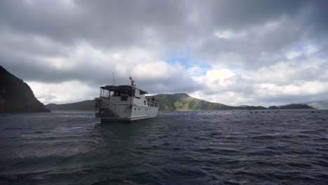 slowmo - barco de crucero con gente pescando anclado en la bahía con colina detrás en nueva zelanda
