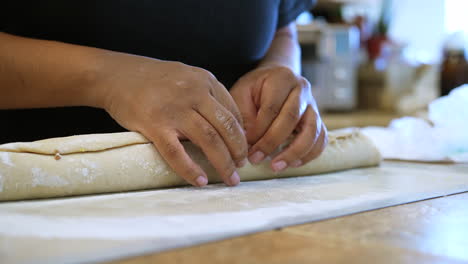 after rolling dough, sugar and cinnamon into a roll, the chef pinches the seam together to press and seal before slicing into rolls