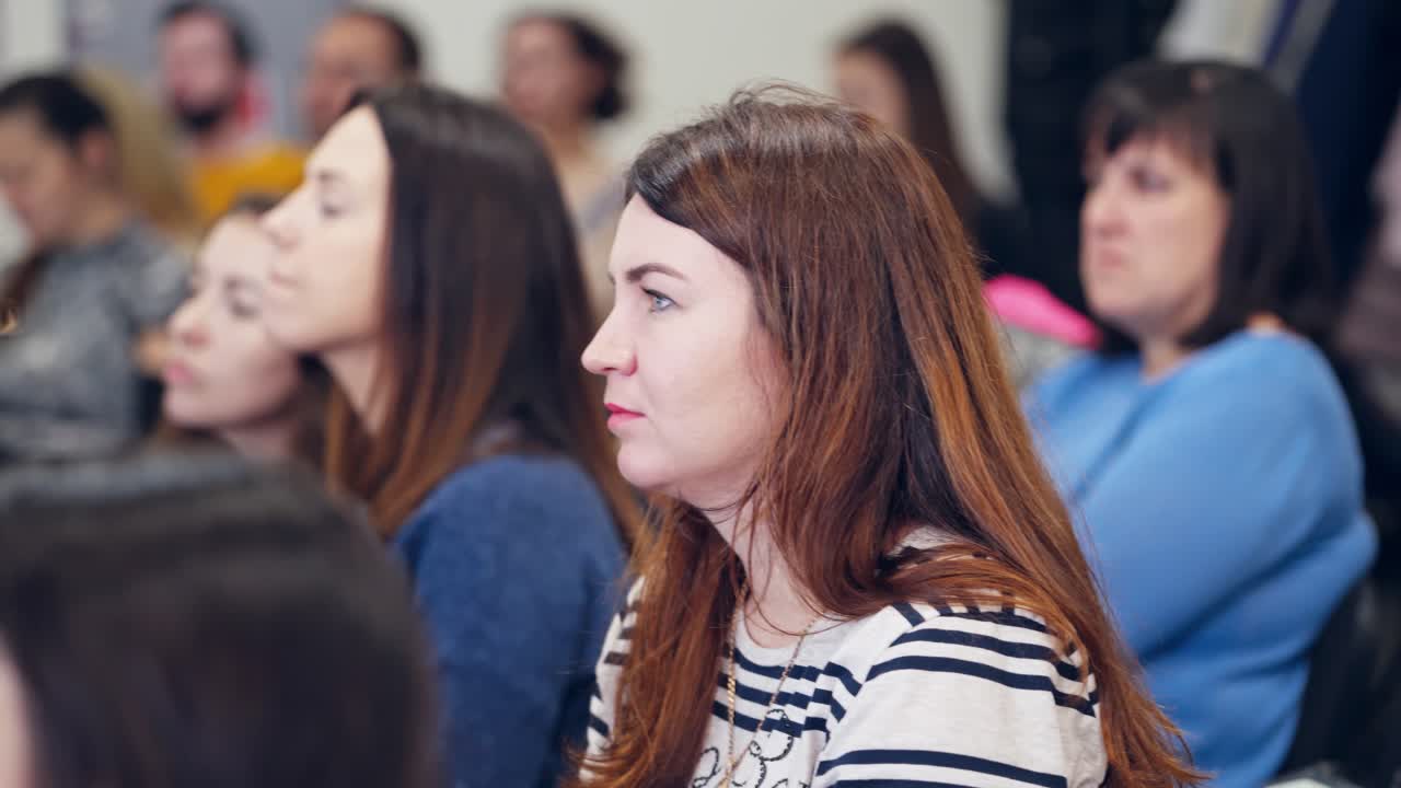 People listening on business forum. Side view of a woman on blur background of female audience sitting in a lecture hall or seminar room.