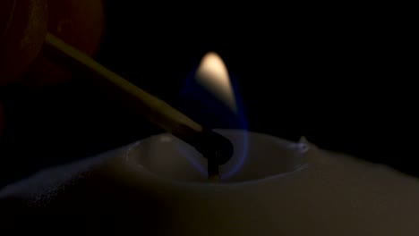 slow motion macro footage of a white candle lit by a match on a dark background