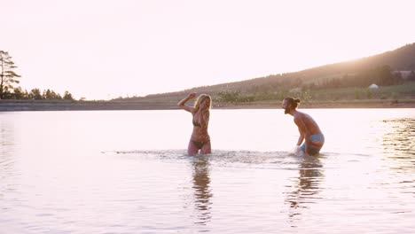 couple having fun splashing in lake backlit by evening sun