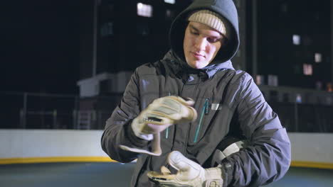 goalkeeper carefully adjusts hand glove with ball securely held under arm during nighttime practice on urban sports field, scene highlights athlete's preparation