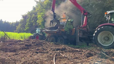 farmer using grabber on end of hydraulic arm to feed wood and vegetation into a shredder