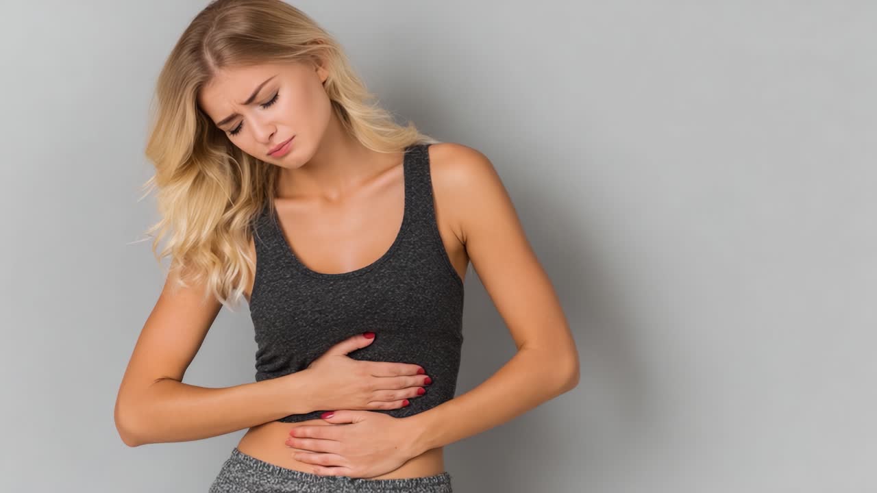 Una donna che esprime disagio mentre si tiene lo stomaco, rappresentando le sensazioni fisiche associate al dolore o al malessere, su uno sfondo neutro per enfatizzare la sua espressione.