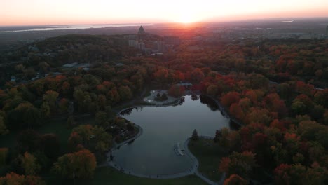 aerial shot over lac des castors in montreal mont royal park with saint joseph oratory in the background at sunset during fall season, montreal city, quebec province, canada