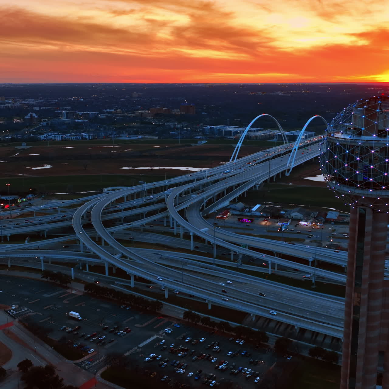Flying along the spherical top of Reunion Tower in Dallas, Texas, USA at sunset. Complicated road system, Dallas Margaret Mcdermott Bridge and city view at the backdrop of orange sky
