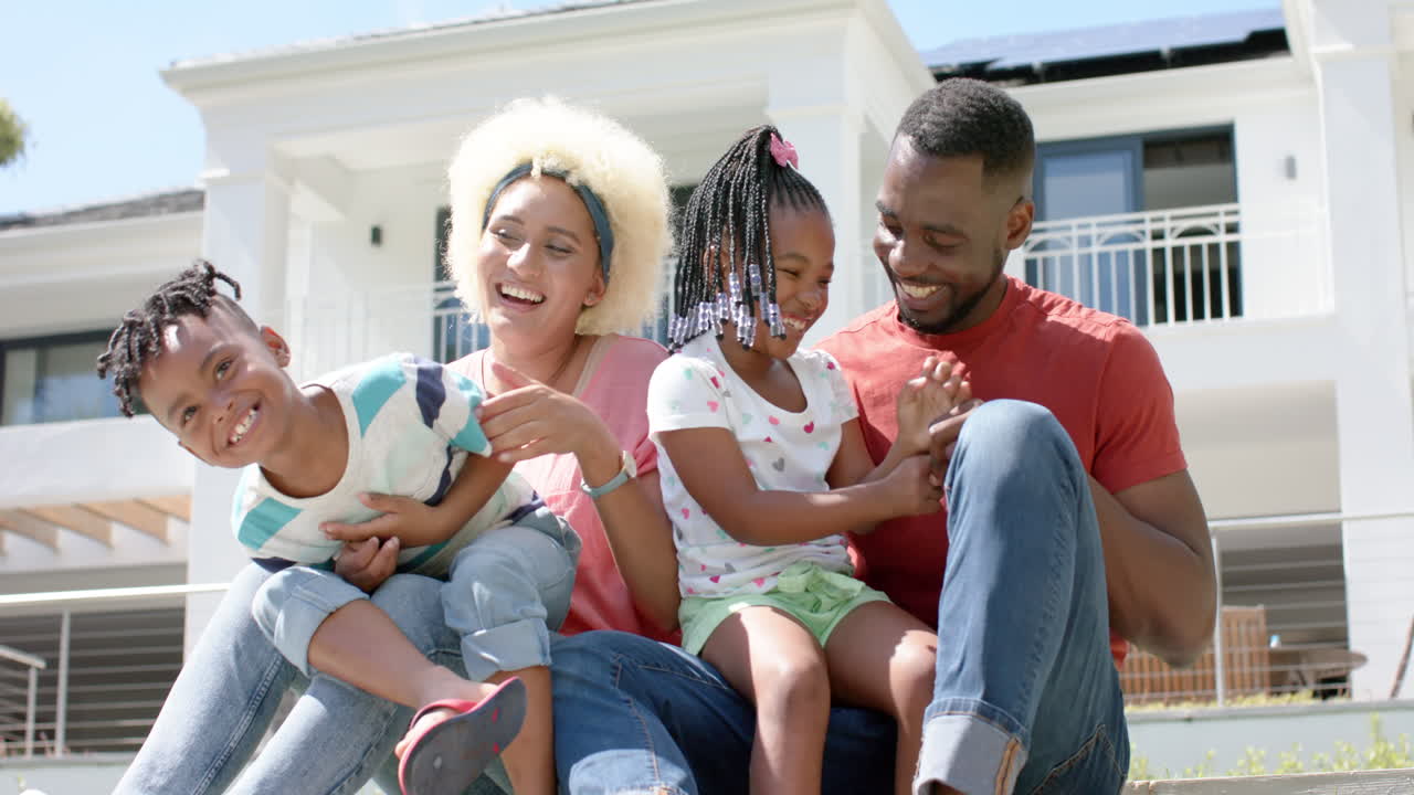 Homem afro-americano, jovem mulher birracial e duas crianças sorriem juntos