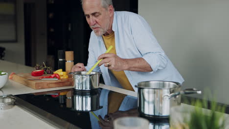 senior man tasting soup in kitchen
