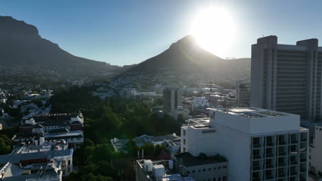 Forwards-fly-above-buildings-and-park-in-city.-View-of-Lions-Head-bright-against-sun.-Cape-Town,-South-Africa