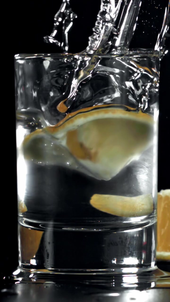 Una fetta di limone cade in un bicchiere d'acqua con schizzi di liquido al rallentatore