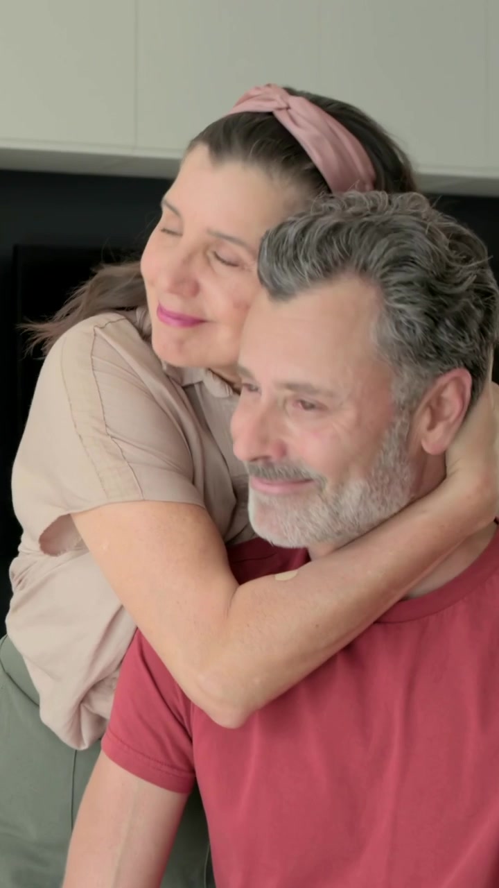 Video verticale: Entrando dietro una donna che abbraccia un uomo seduto con un orologio a casa, mostrando affetto