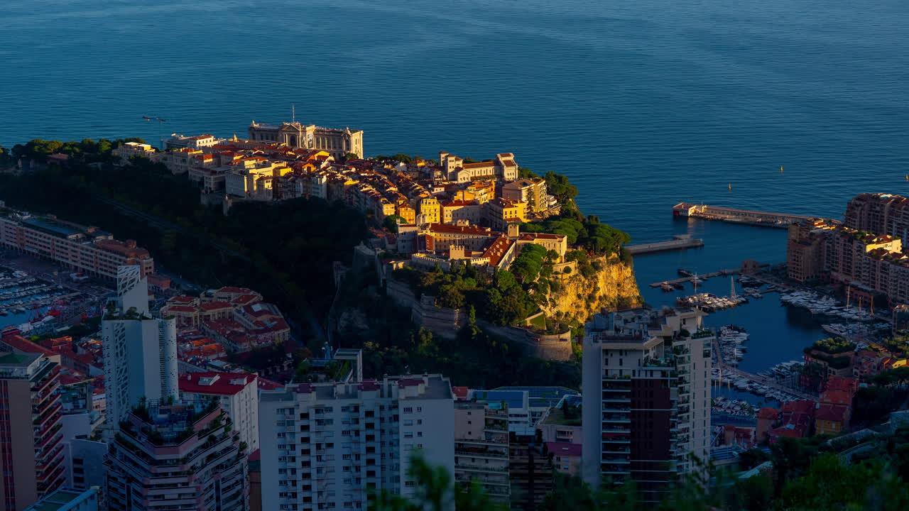 Timelapse al tramonto dall'alto di Monaco-Ville sulla roccia, fiancheggiata da Port Hercule e Fontvieille. La luce del sole sfuma in un crepuscolo profondo sul Mediterraneo.