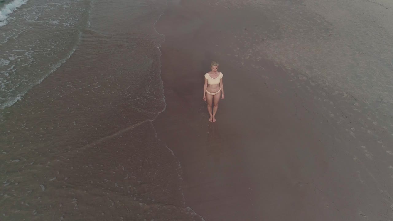 vista aérea de una atractiva mujer rubia en bikini parada en la playa