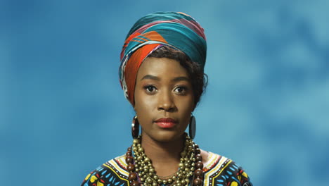 african american young woman in turban and traditional clothes looking with serious expression at camera