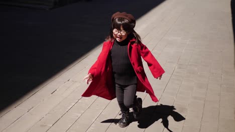 fashionable korean baby girl in a red coat walks down the street in spring