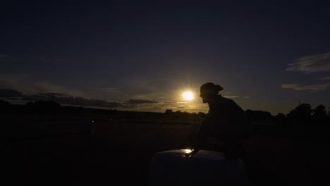 the silhouette of a man doing a hand stand on top of a ball of hay in the sunset