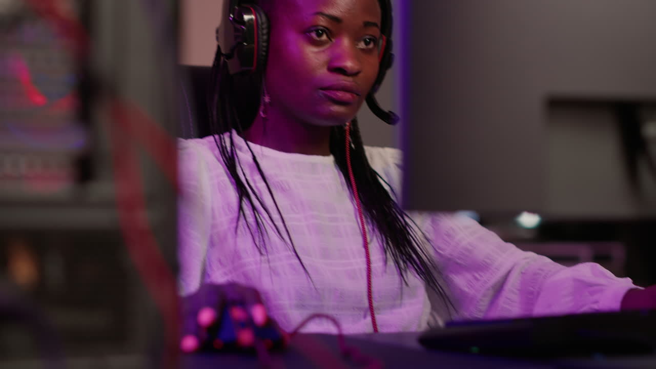 Handheld shot of african american gamer girl with professional pc setup using gaming headset talking to team