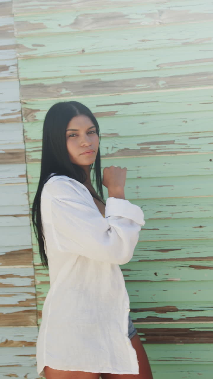 Vertical video portrait of biracial woman dancing against weathered wood wall in sun, slow motion