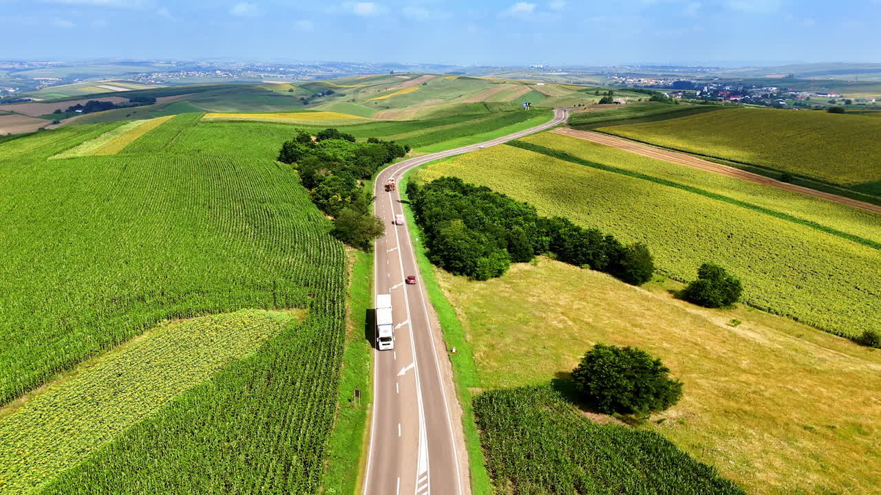 Trucking along winding road through green farmland landscape. A truck drives along a curvy road surrounded by vibrant green fields and hills under a clear blue sky