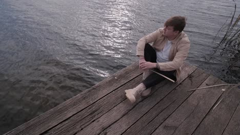 young man lies alone on wooden footbridge and staring at lake. thinking about life. peaceful atmosphere in nature. enjoying fresh air. back view.