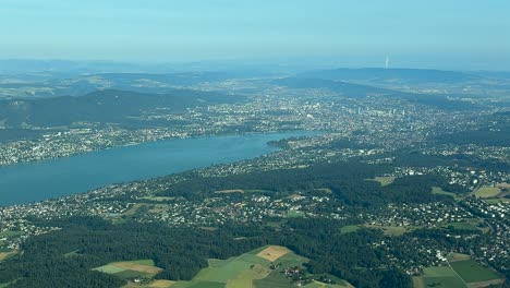 An elevated aerial view of Zurich city and lake, taken from an airplane cockpit in a hazy summer morning