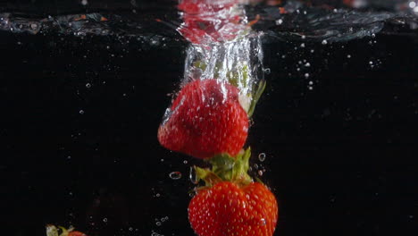 cámara lenta fresca hermosas fresas caen en el agua con burbujas