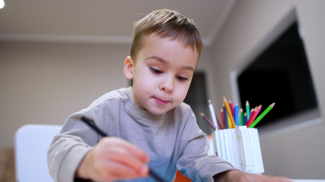 Bambino ama il divertimento del disegno al chiuso! Bambino piccolo impegnato nell'arte, concentrato a colorare un foglio di carta a un tavolo in un ambiente interno accogliente.