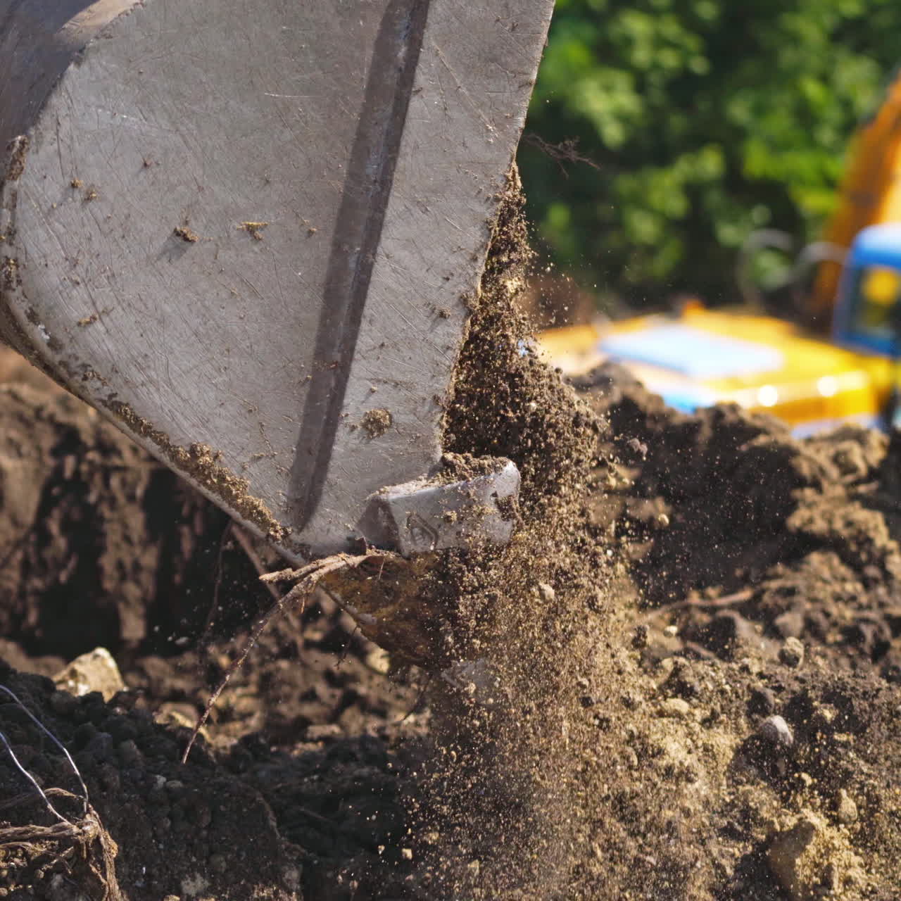 Bucket of tractor digs the ground. Excavator digging the soil on the background of green trees in summer. Close-up.