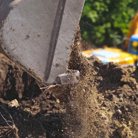 bucket of tractor digs the ground. excavator digging the soil on the background of green trees in summer. close-up.