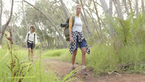 una joven caucásica conduce el camino en una caminata por el bosque, con una joven de dos razas siguiendo