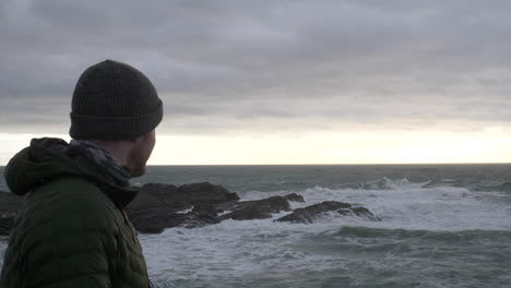 Man-Wearing-Winter-Clothes-Overlooks-Stormy-Sea-At-Sunset