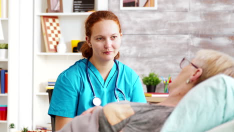 Revealing-shot-of-female-assistant-talking-with-an-old-lady-lying-in-hospital-bed