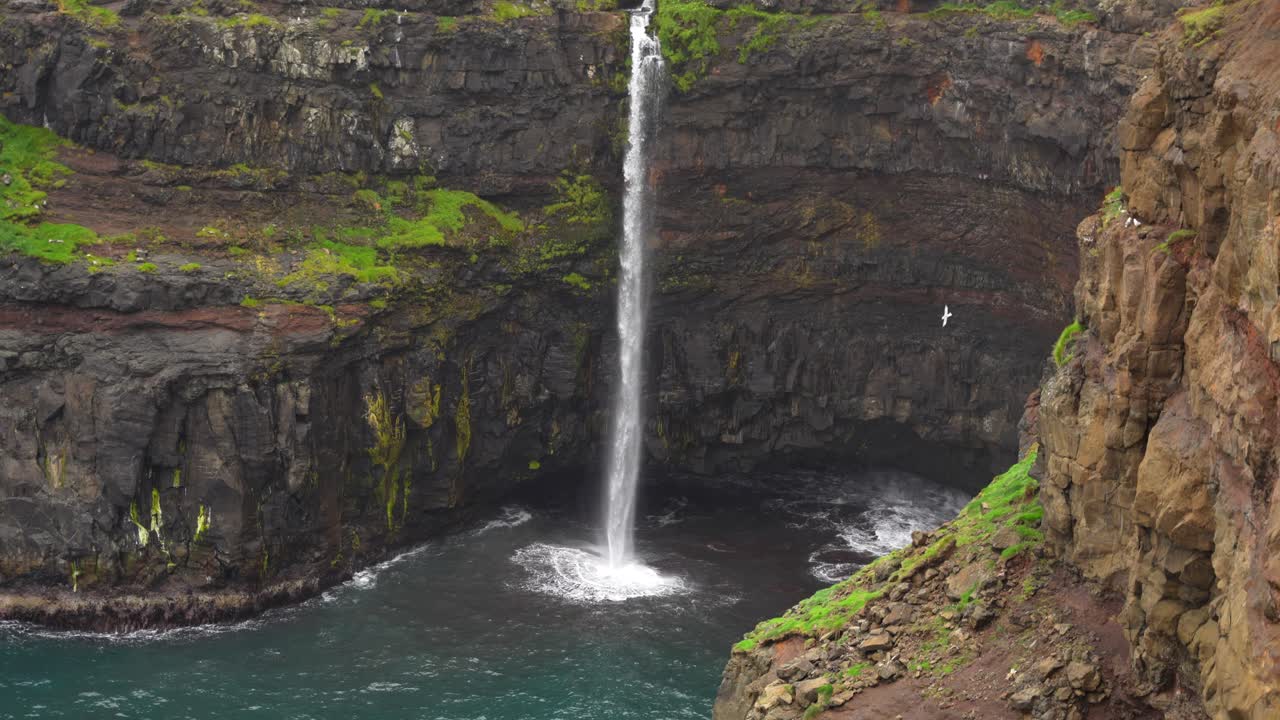 cascada de mulafossur desde la parte superior con el pueblo de gasadalur en el fondo y una gaviota volando alrededor