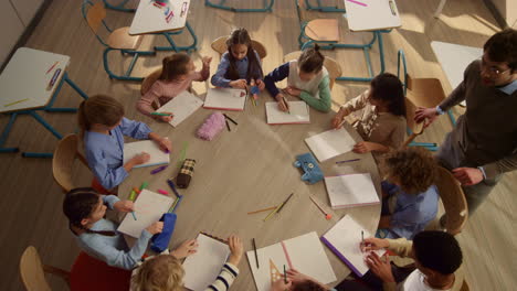 mixed race children having lesson with teacher at round desk