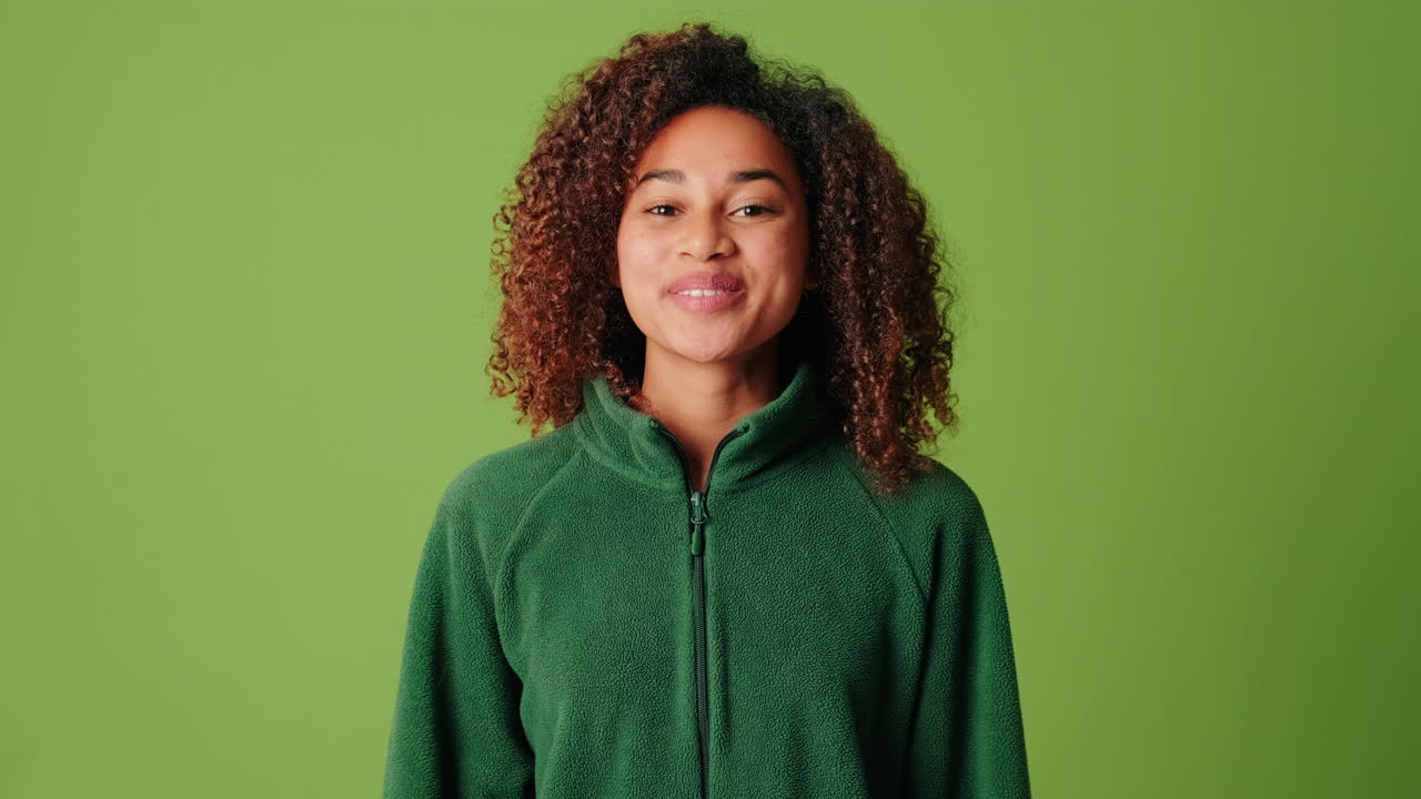 Giovane donna afroamericana che saluta e sorride su schermo verde.
