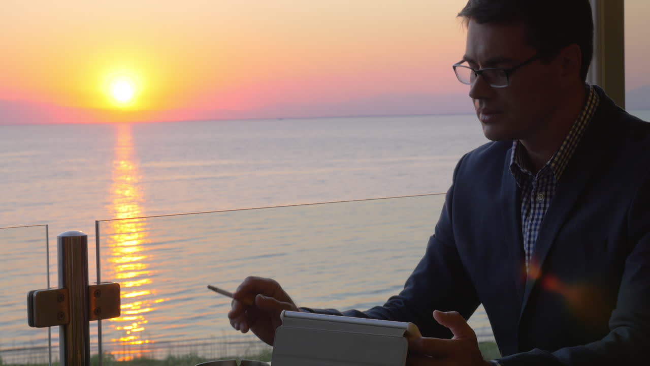 hombre de negocios fumador trabajando con un touchpad en un café junto al mar