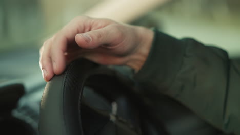 close-up of a man's hand resting on the steering wheel of a car. the man is wearing a green jacket, indicating a moment of stillness and focus, possibly preparing for a drive