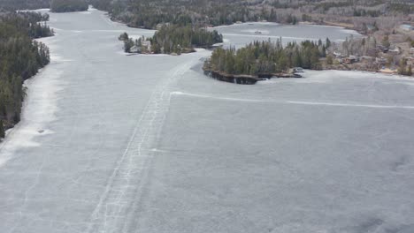 aerial circle left over melting frozen lake with cracks in the ice roads still visible in canada