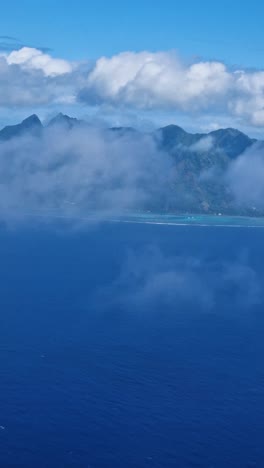 vertical view of moorea island, french polynesia coastline behind clouds, airplane passenger point of view