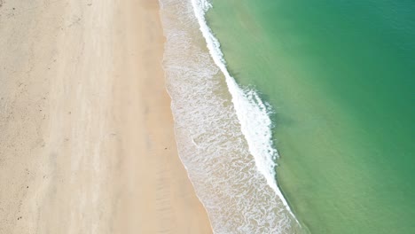 Waves-of-emerald-colored-sea-breaking-on-golden-sandy-beach