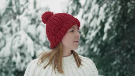 caucasian woman wearing red hat walking in snowing forest.