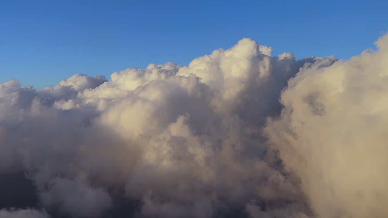 An immersive pilot’s eye view from a jet cockpit while flying through cottony small storm clouds illuminated by the sunset warm light. Ultra-realistic 4K shot